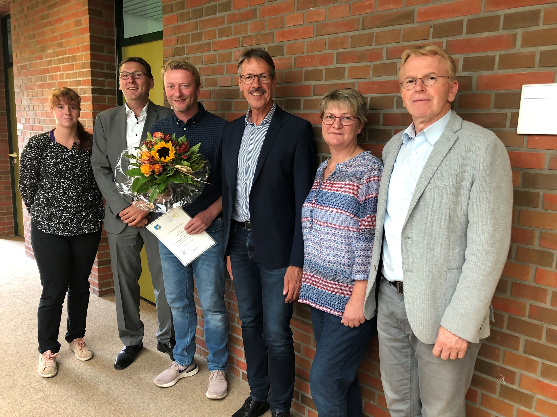 Der Jubiliar steht zusammen mit dem Bürgermeister und dem Ersten Gemeinderat sowie drei Mitarbeiter des Fachbereiches vor einer Wand im Obergeschoss desRathaus 