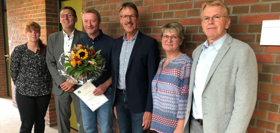 Der Jubiliar steht zusammen mit dem Bürgermeister und dem Ersten Gemeinderat sowie drei Mitarbeiter des Fachbereiches vor einer Wand im Obergeschoss desRathaus 