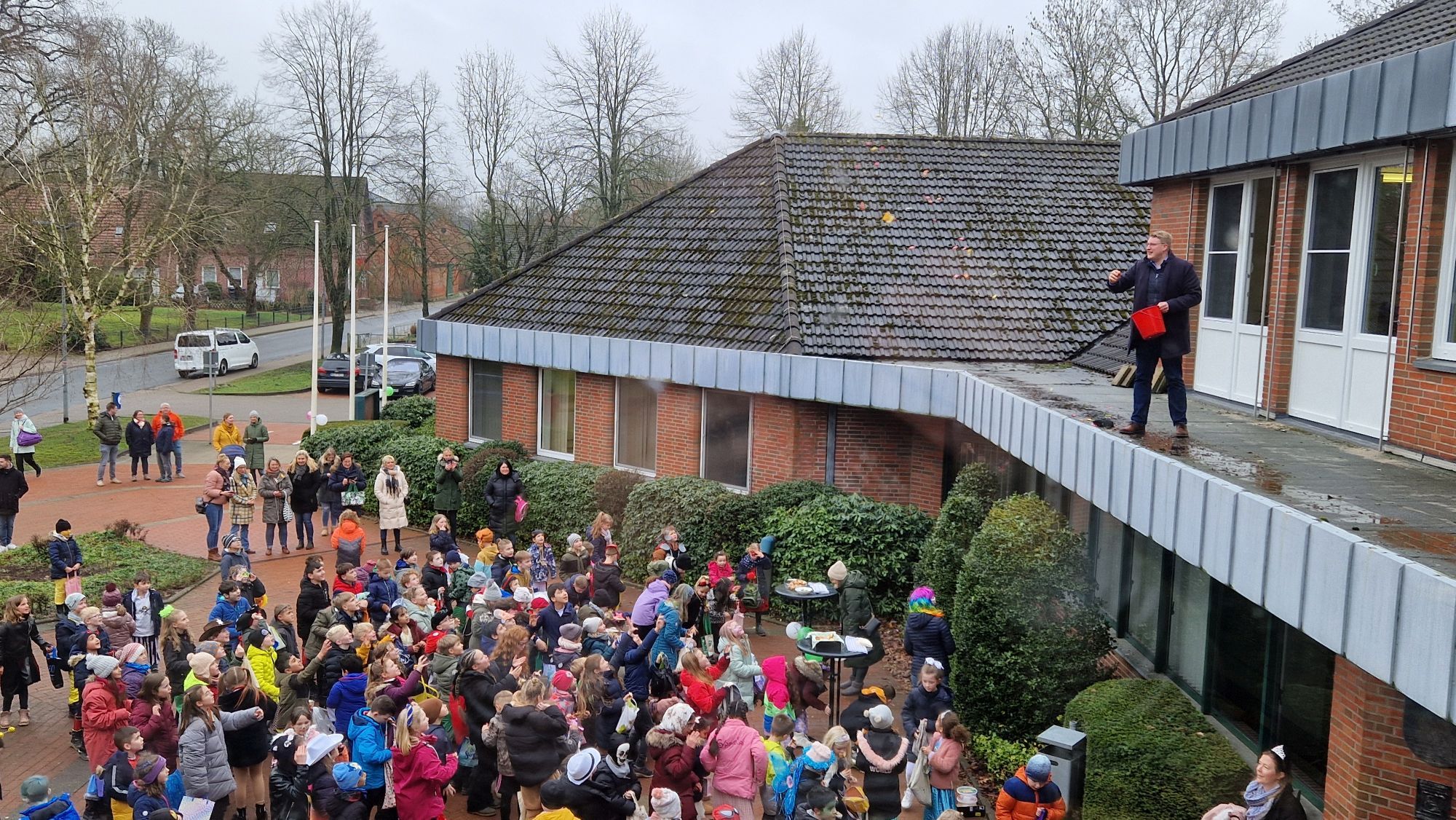 Bürgermeister Henrik Wärner wirft Bonbons vom Vordach für die Schüler der Grundschule Schiffdorf